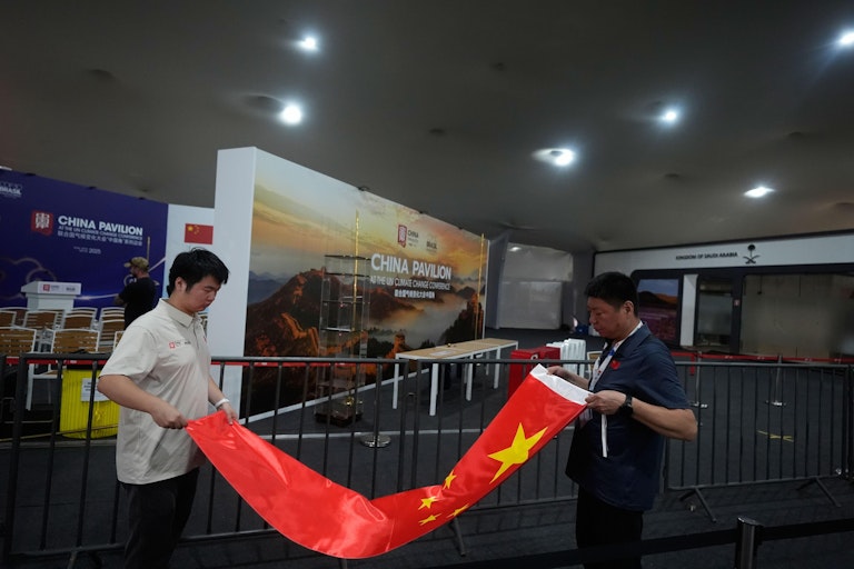 Two men rolling up a Chinese flag in front of the China stand at COP30.