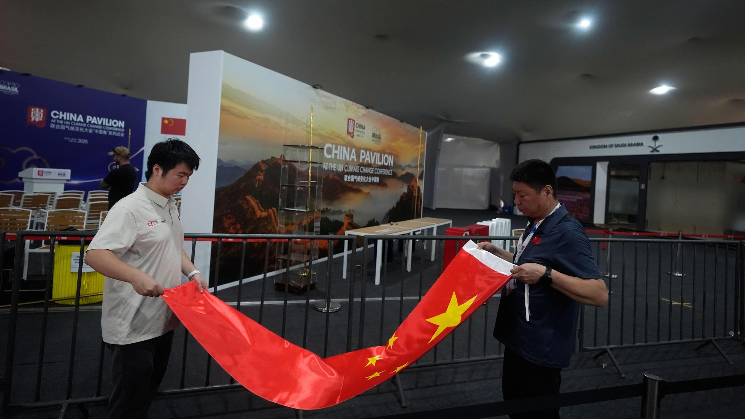 Two men rolling up a Chinese flag in front of the China stand at COP30.