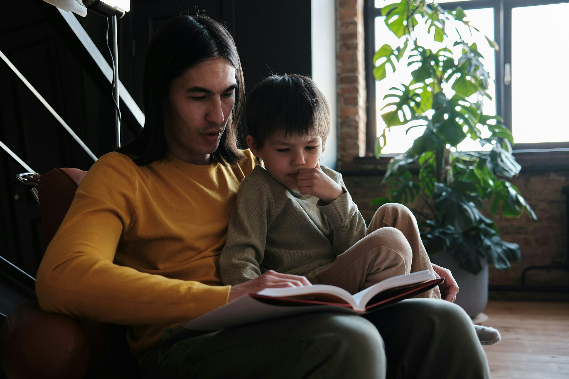 An adult sitting in a chair with a little boy and a book.