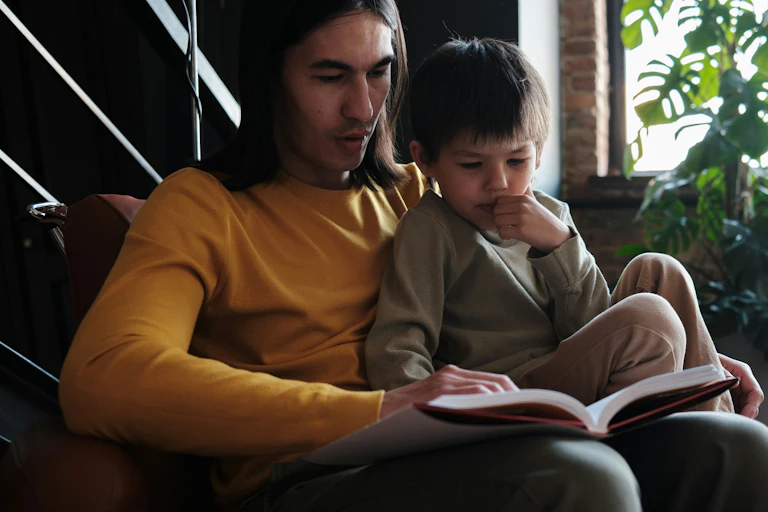 An adult sitting in a chair with a little boy and a book.