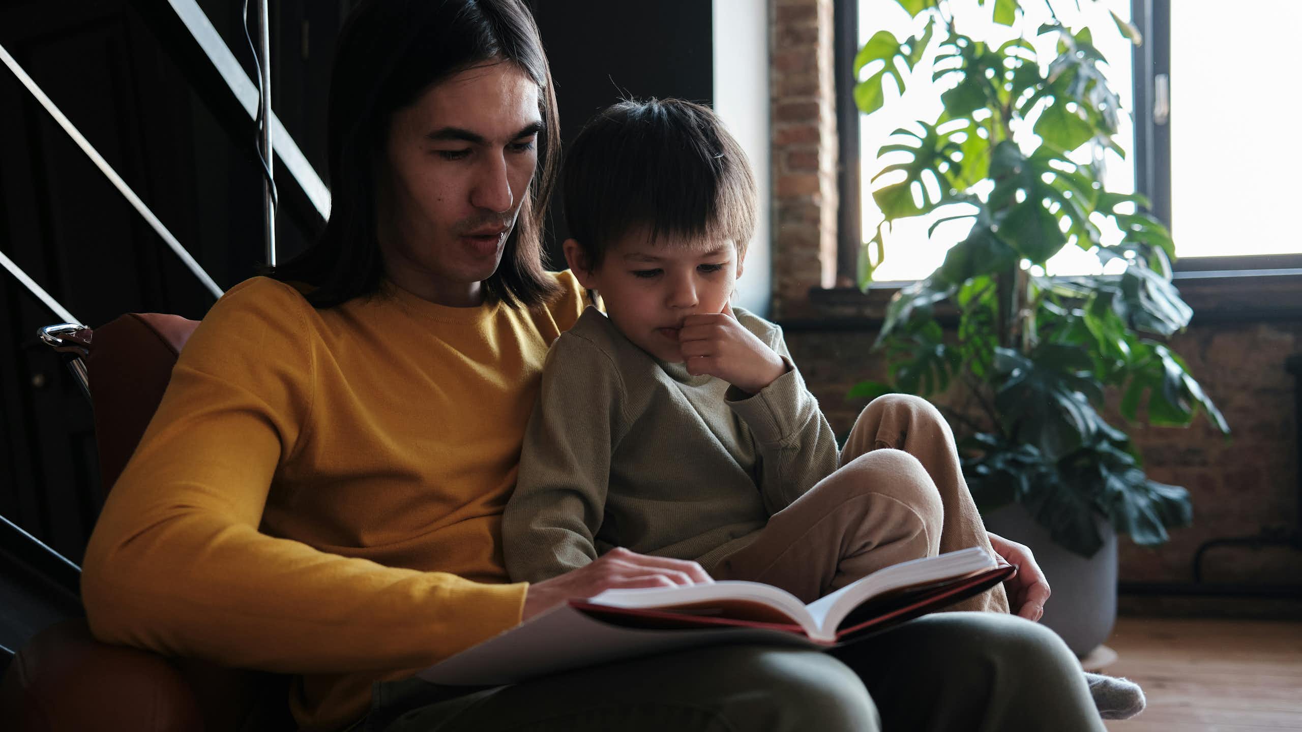 An adult sitting in a chair with a little boy and a book.