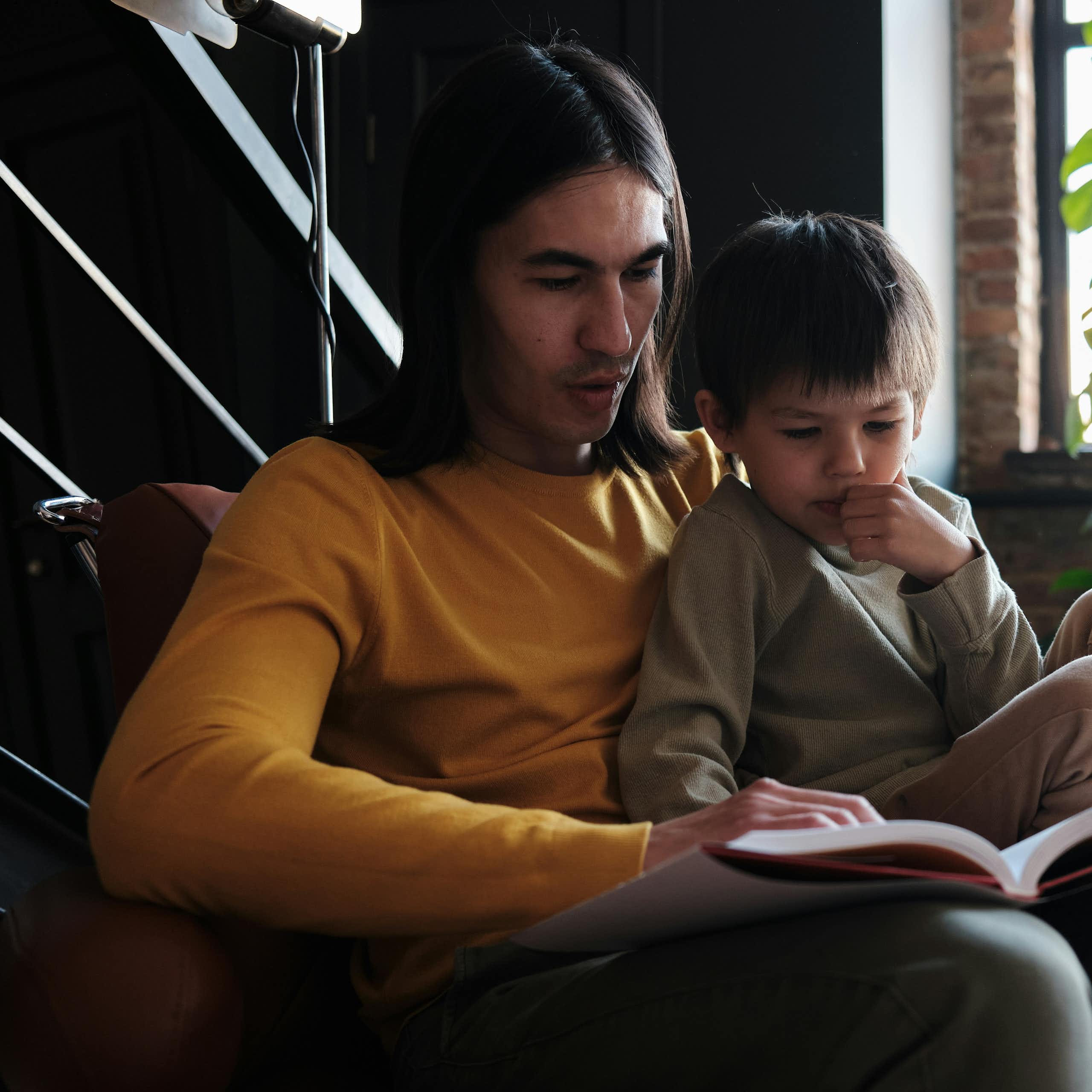 An adult sitting in a chair with a little boy and a book.