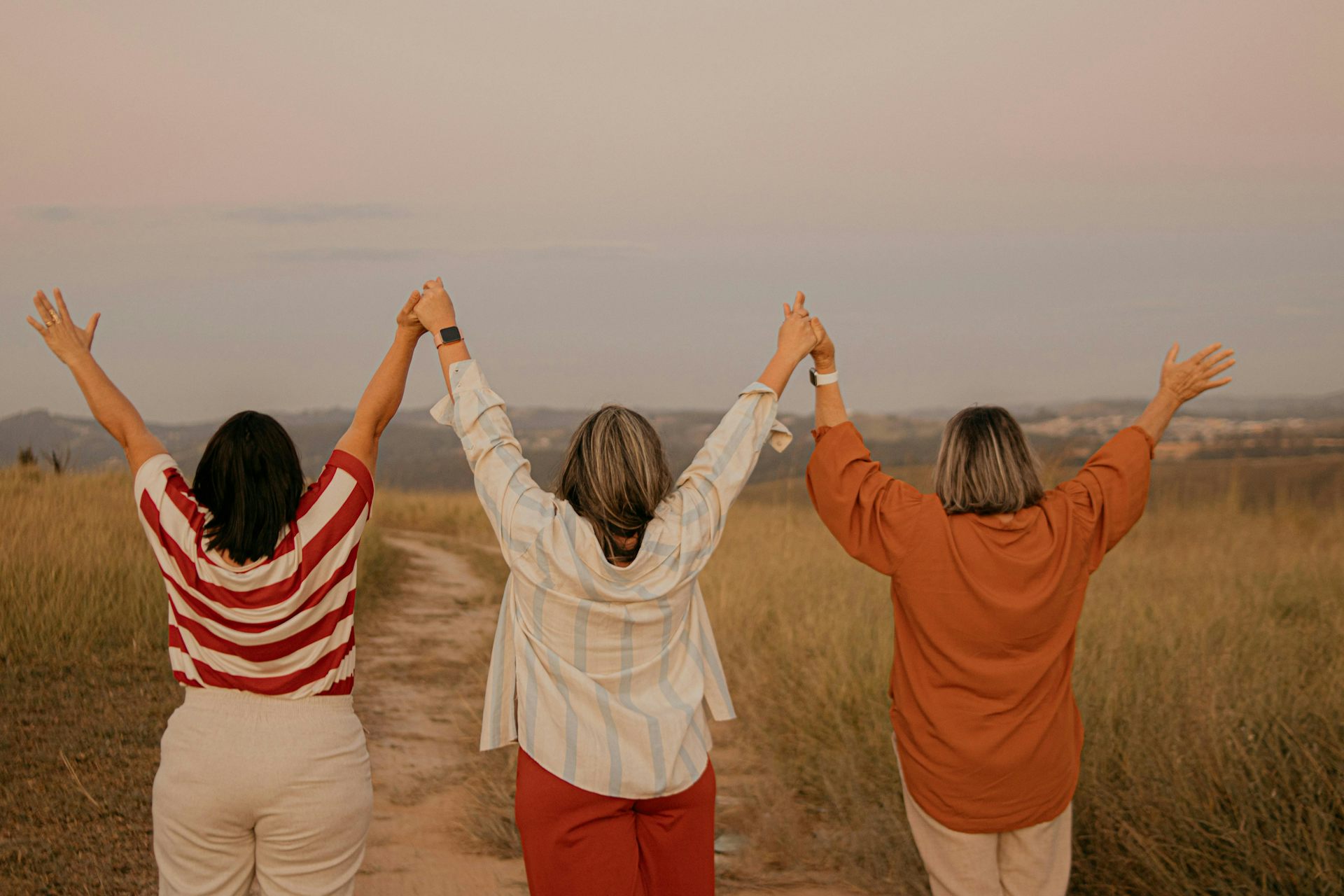 Tres mujeres al aire libre con los brazos levantados, vistas desde atrás