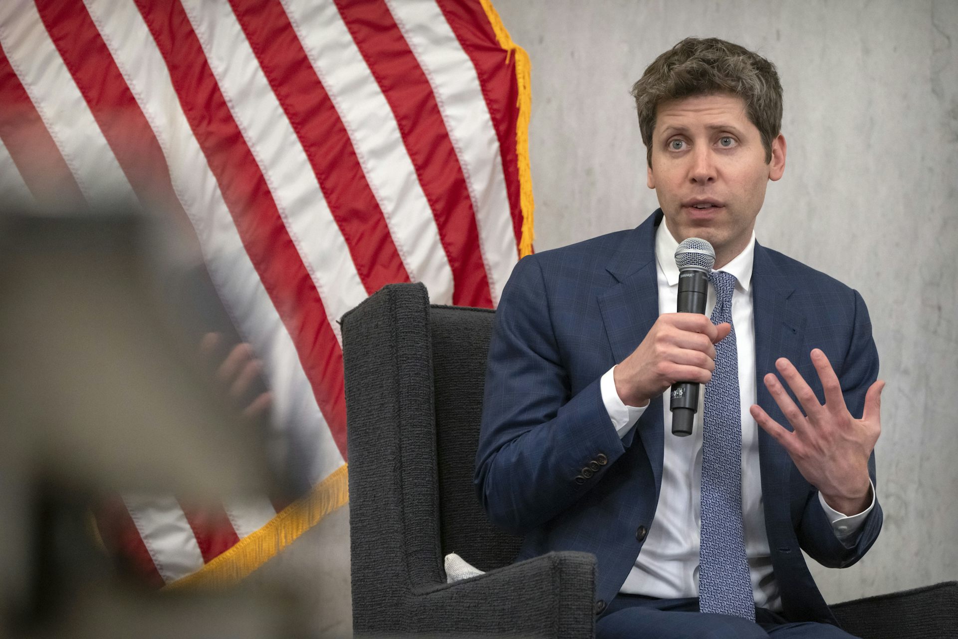 Un hombre blanco de mediana edad con traje habla por un micrófono al público.