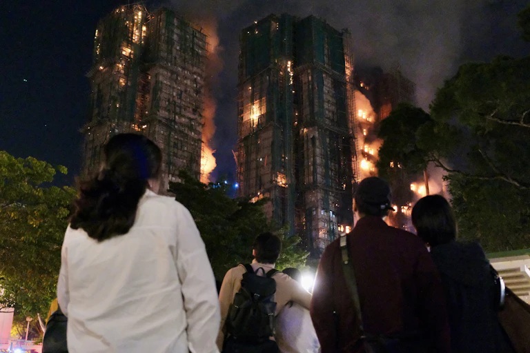 People seen from the back at night watching the apartment block blaze.