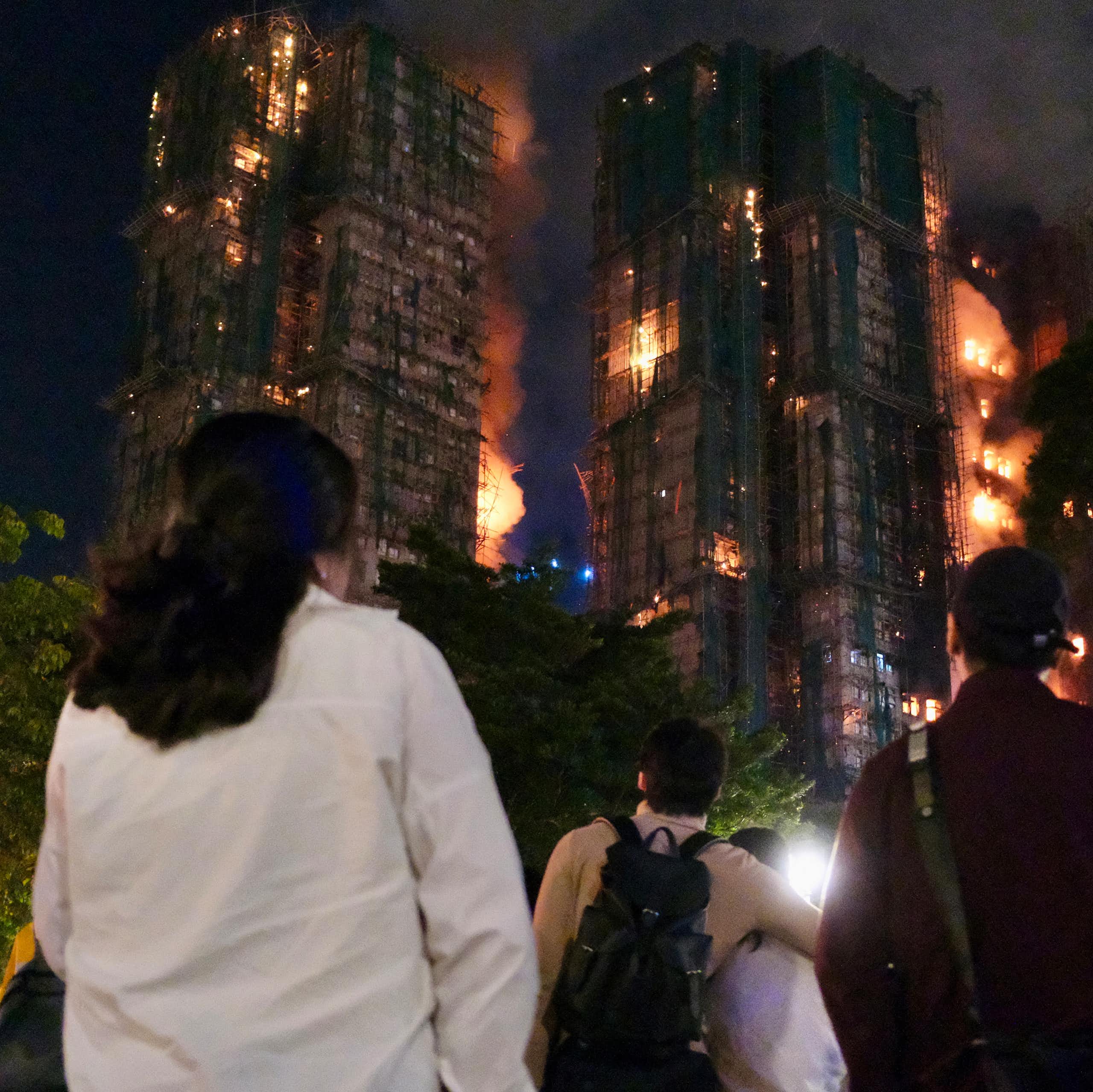 People seen from the back at night watching the apartment block blaze.