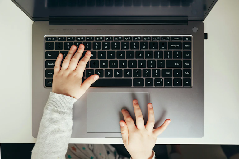 A child types on a laptop keyboard.