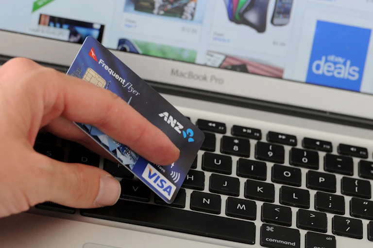 A hand holding a credit card in front of a screen showing products on sale.