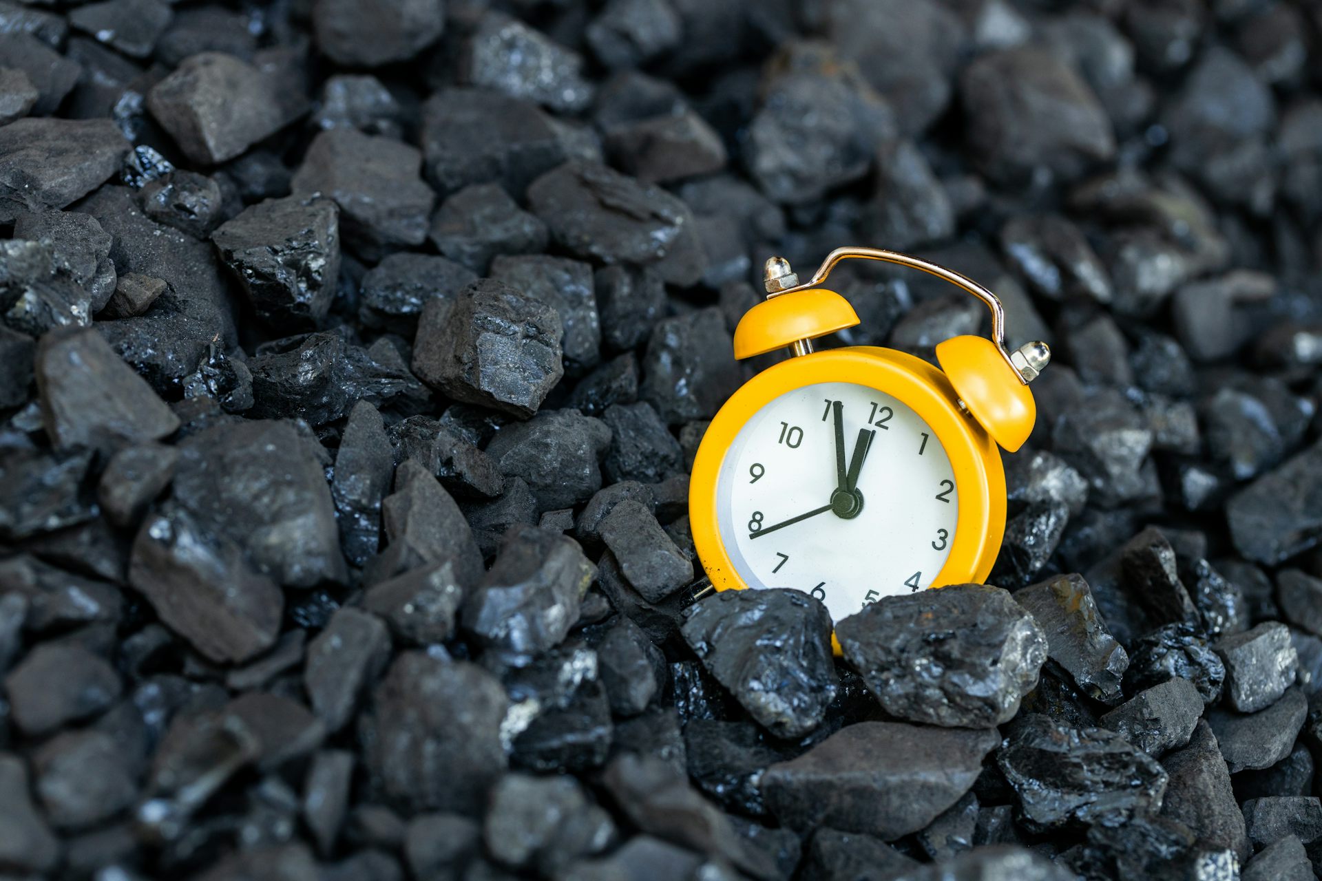 yellow clock on bed of black coal