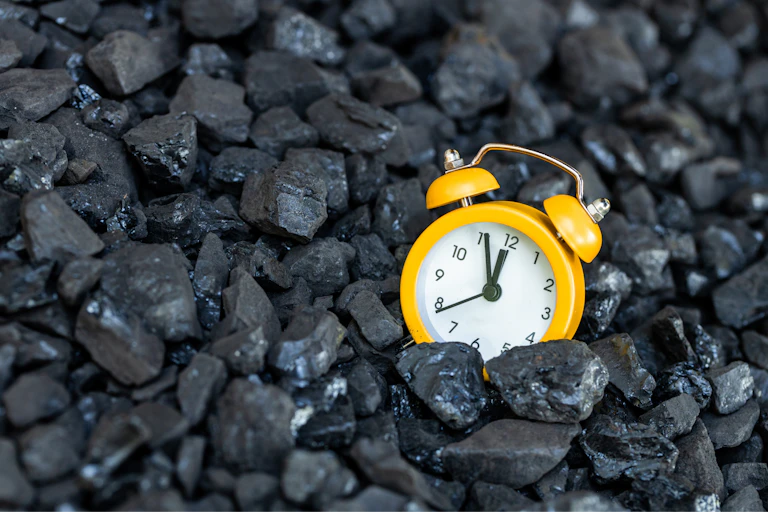 yellow clock on bed of black coal