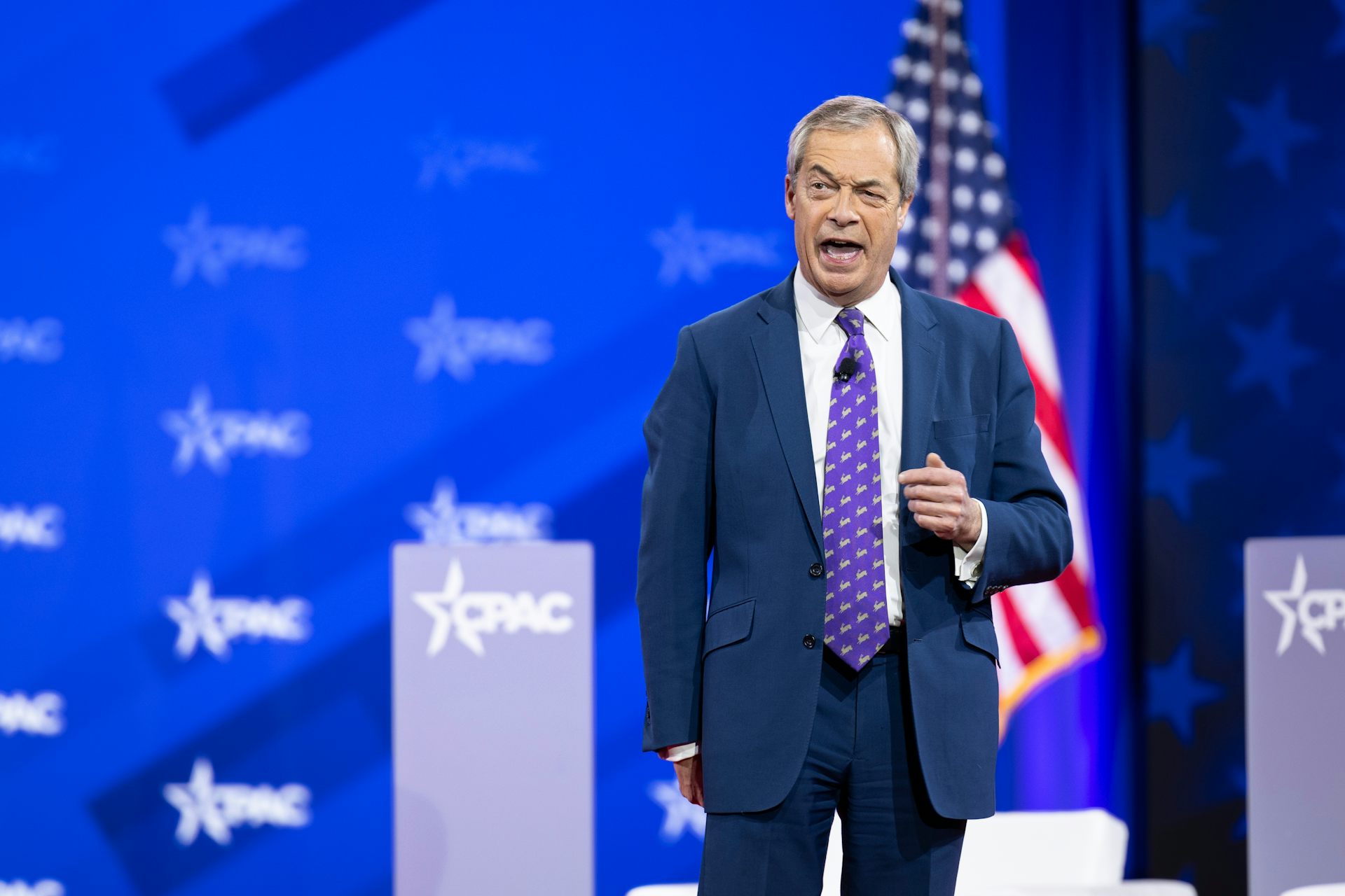 Farage speaking in front of an American flag and CPAC background.