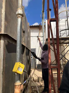 A person taking the temperature of water coming through steel pipes outside a factory