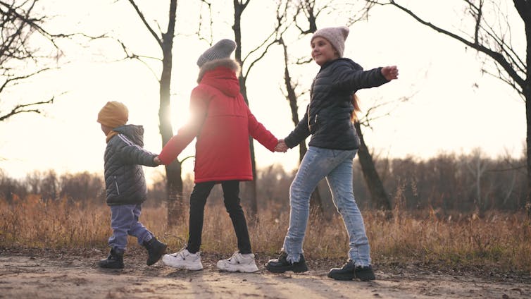 three children holding hands and playing in a forest