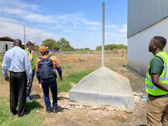 A group of people standing around a steel pyramid shaped structure with a steel pipe coming out the top