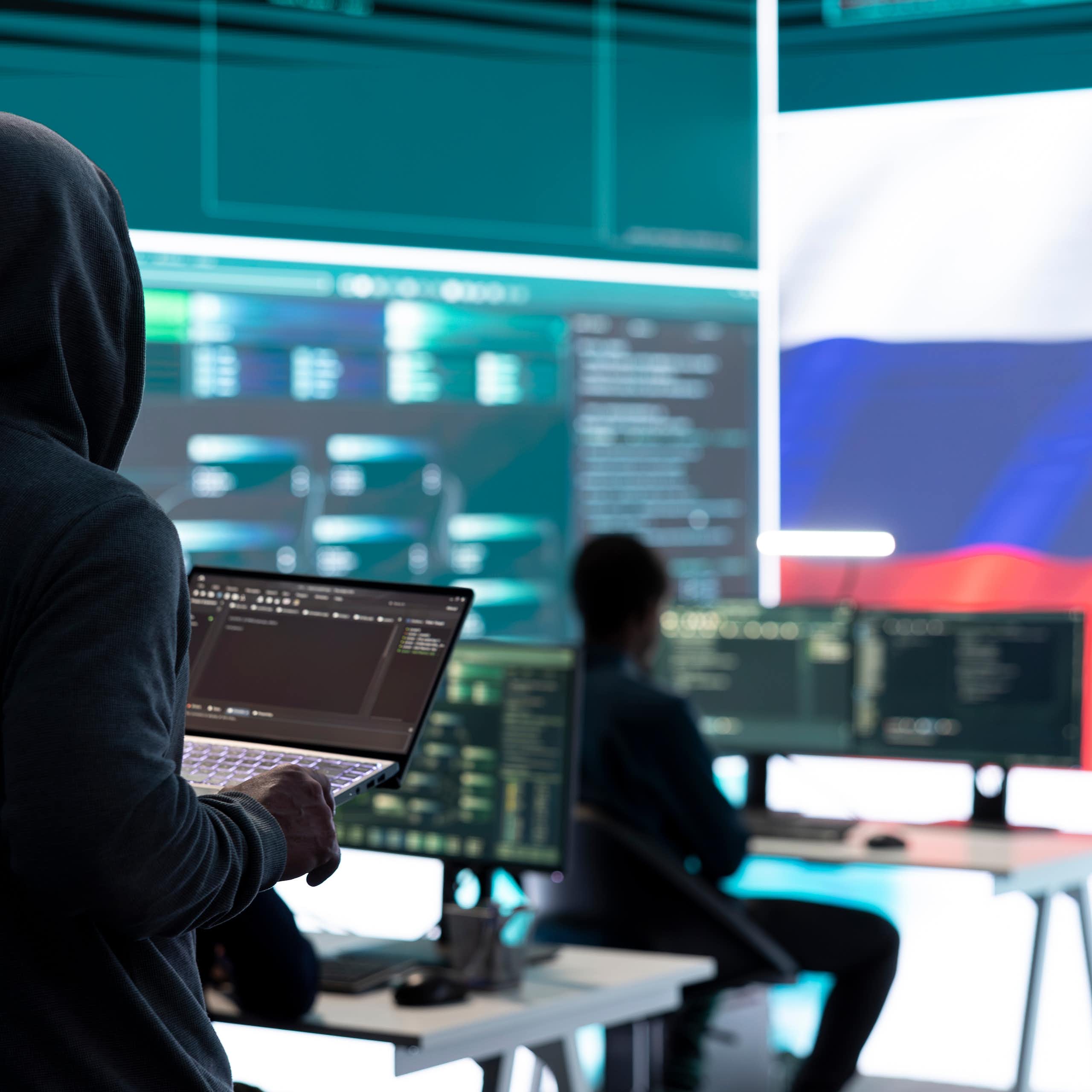 Un hacker sostiene un portátil en una sala con la bandera de Rusia al fondo
