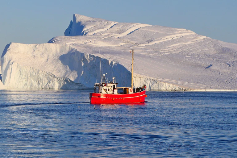A small red boat with icebergs behind it.