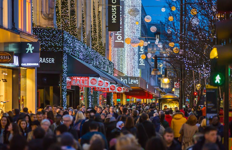 christmas shoppers crowded on a uk high street with lights and decorations.