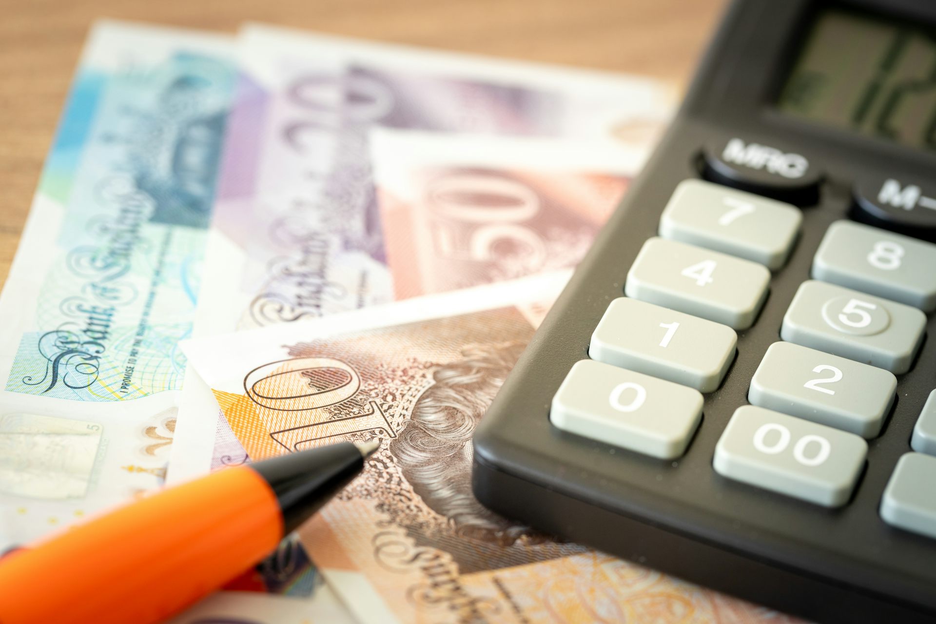 a calculator, a pen and an array of uk banknotes.