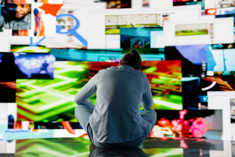 A man sitting dejectedly in front of a huge screen full of colourful images