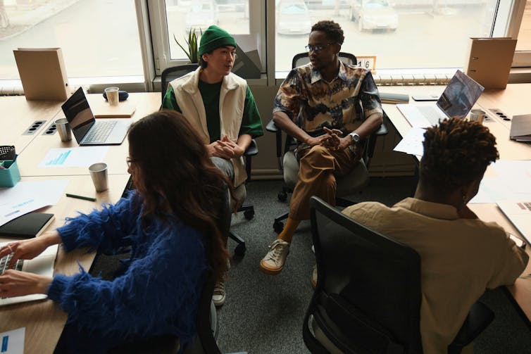 El futuro del trabajo, según la Generación Z, es decidido, digital y flexible 1 Cuatro jóvenes oficinistas están sentados en sus escritorios y hablando entre ellos.