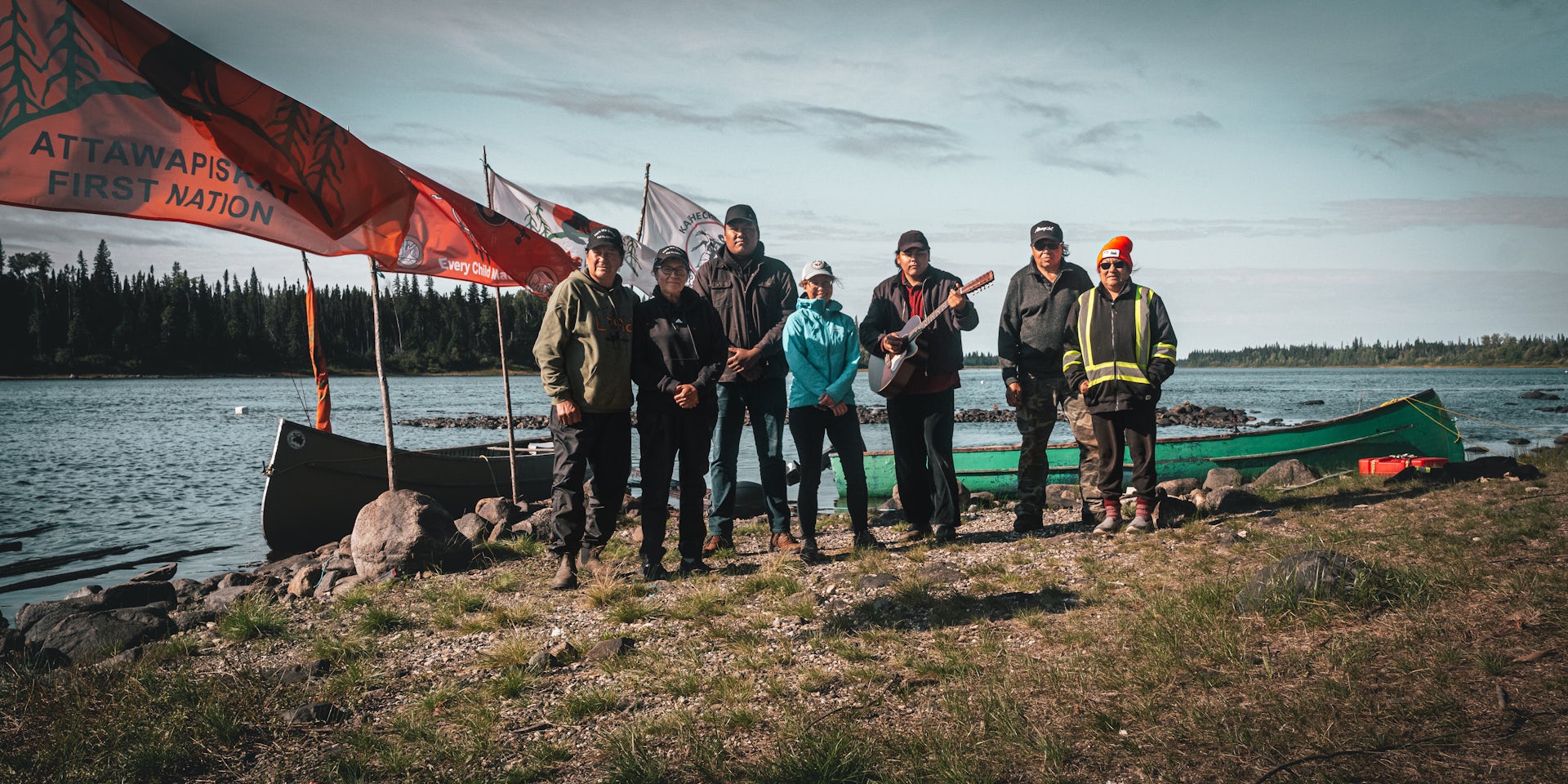 a group of people stand posing for a photo near a body of water. Flag fly of poles behind them