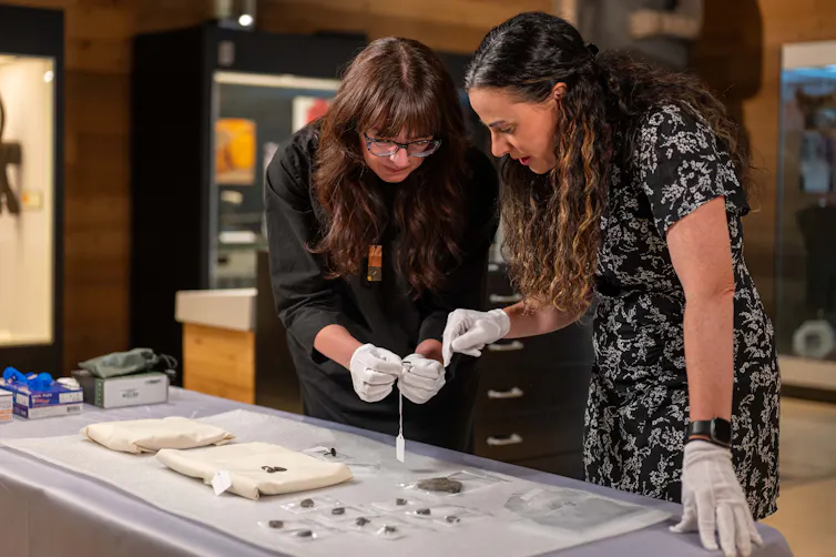 Two women stand at a table examining objects.
