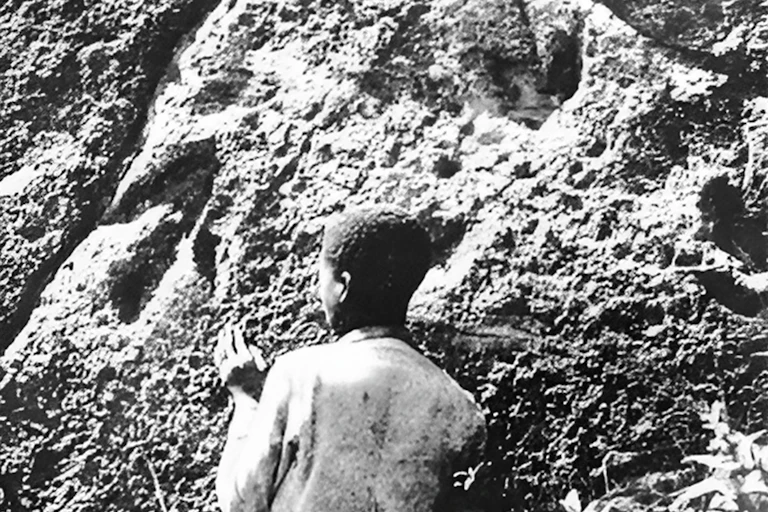 Black and white photo of person looking at rock face that has three-pointed impressions