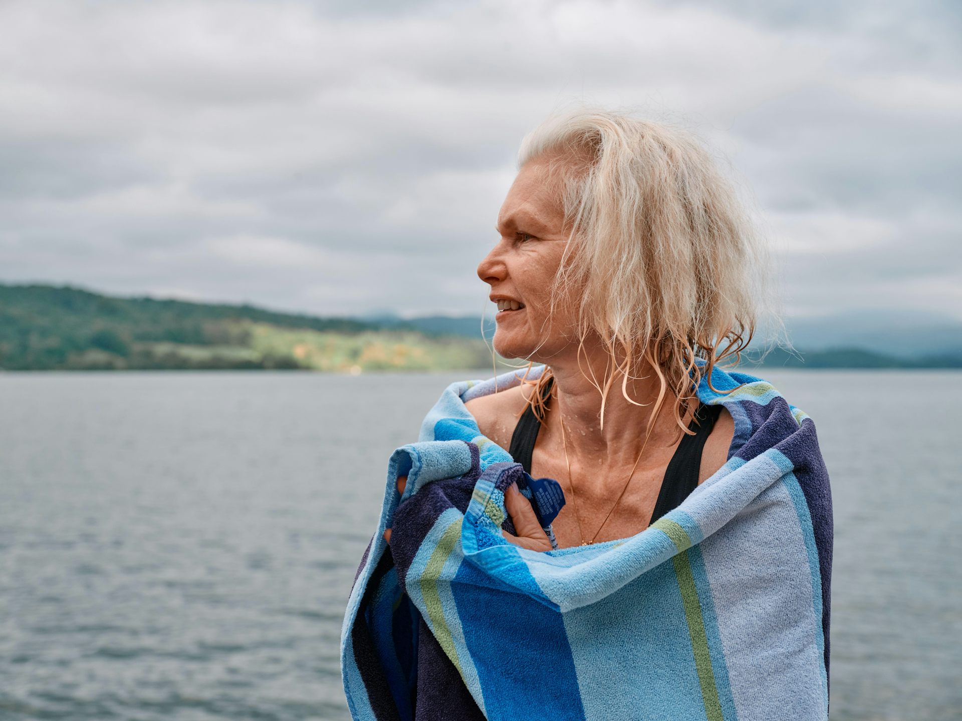 An older woman wraps herself in a towel in front of an expansive lake