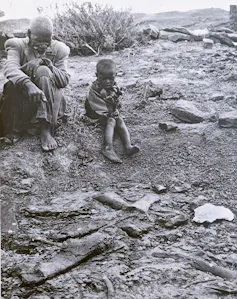 Old man and child sit looking at bones, in an old black and white photo