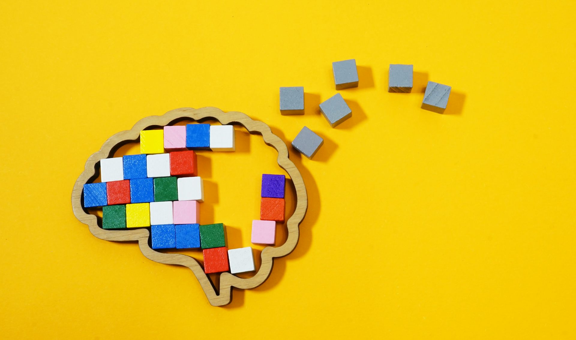 A brain outline with coloured bricks on the inside and grey ones on the outside, against a bright yellow background.