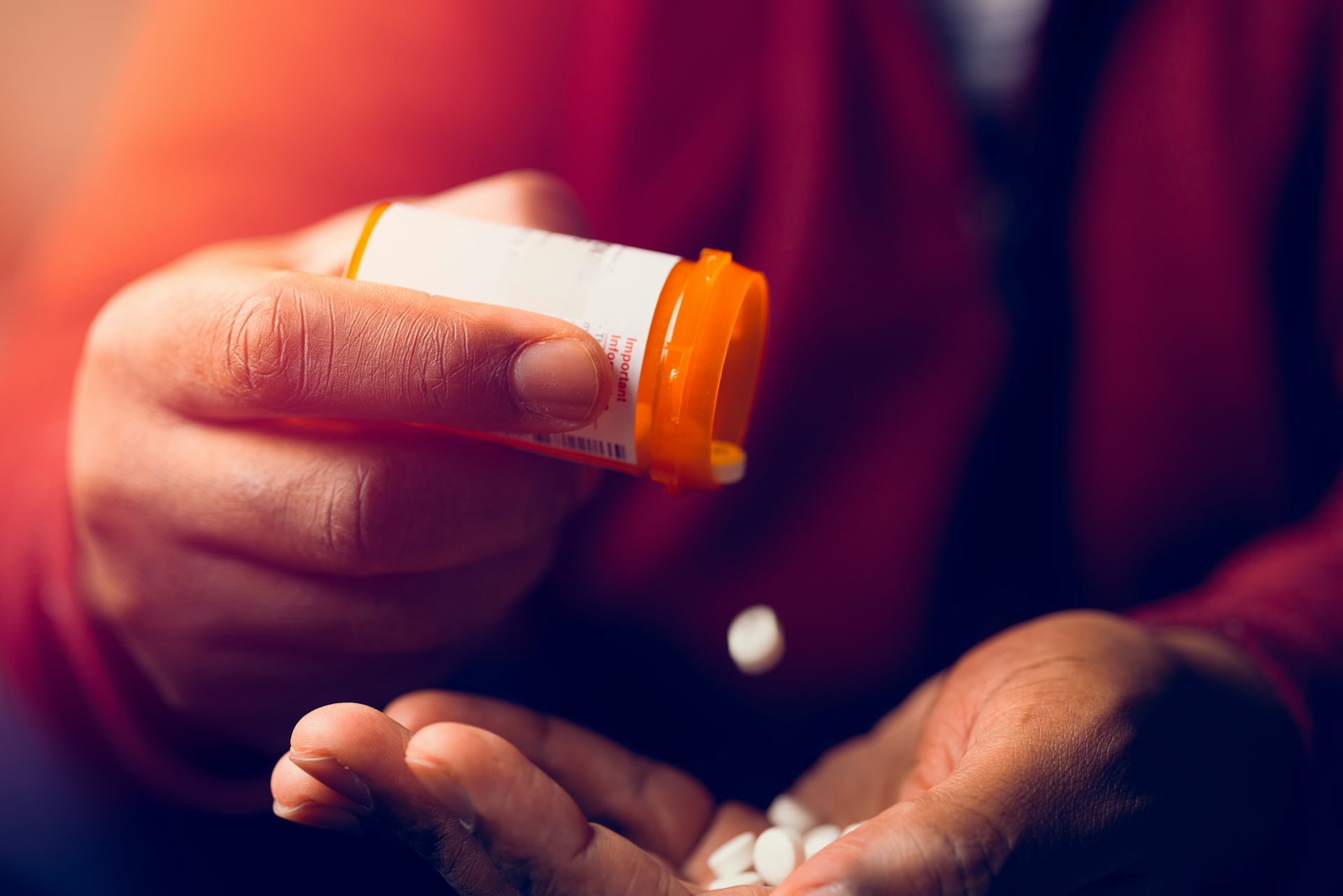 A person pours pills from a prescription bottle into the palm of their hand.