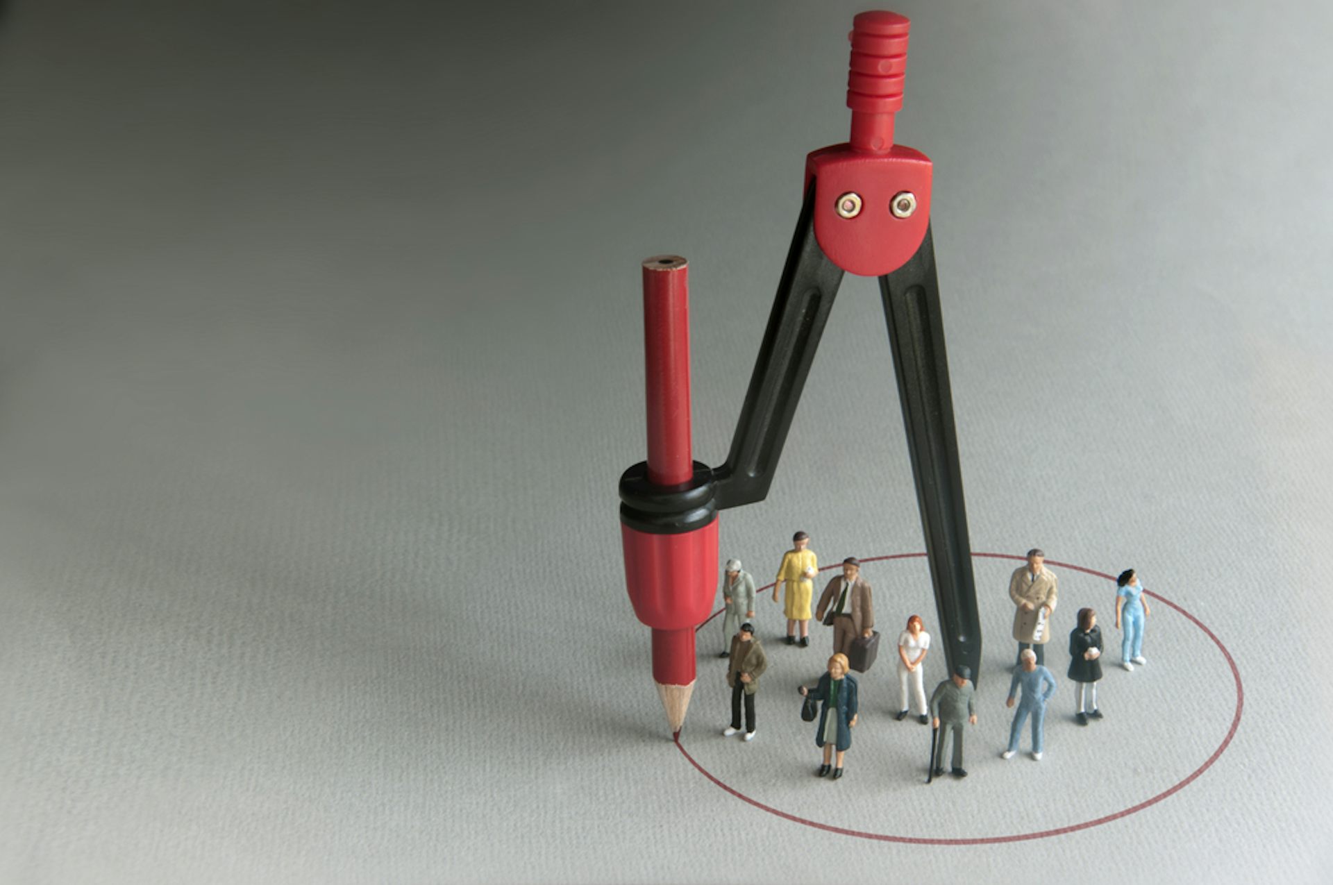 A compass drawing a circle around a group of human figurines.