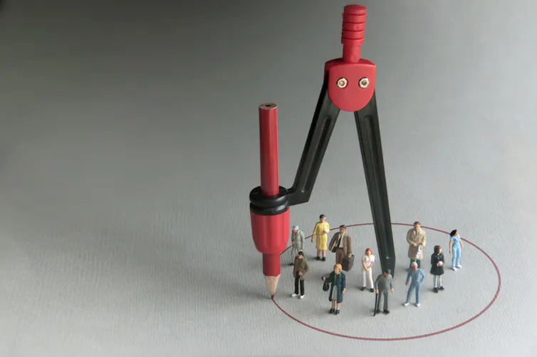 A compass drawing a circle around a group of human figurines.