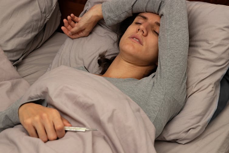 Woman lying in bed with a fever, holding a thermometer.