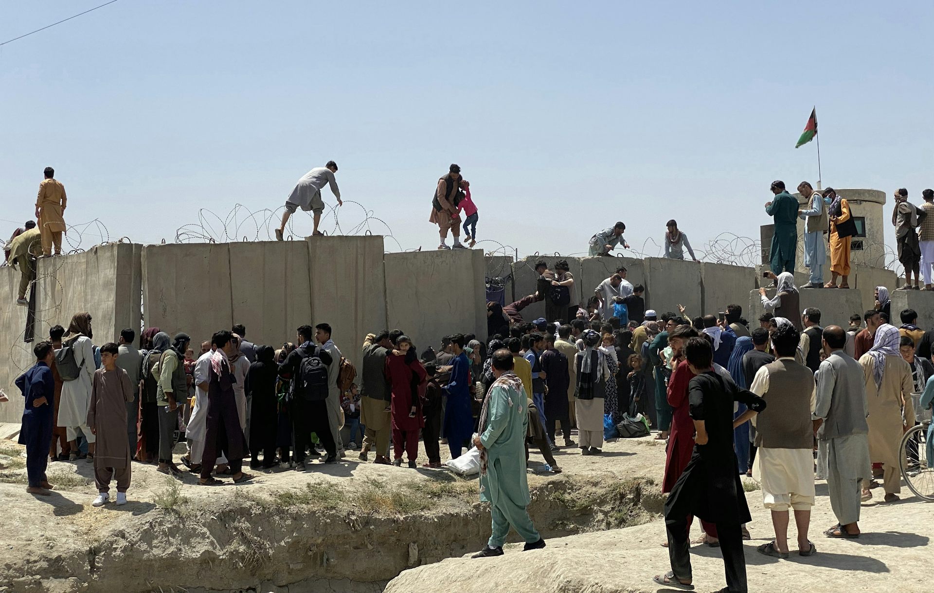 People struggle to cross the boundary wall of an airport in Afghanistan.