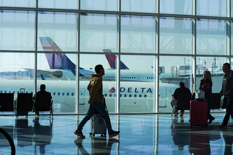 homme qui marche dans un aéroport devant des baies vitrées avec un avion en fond