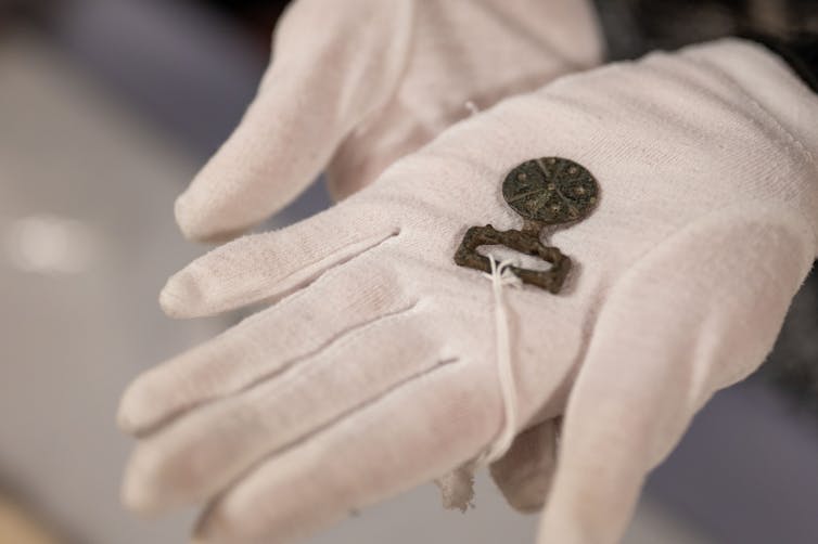 A small medallion held with hands in white gloves.