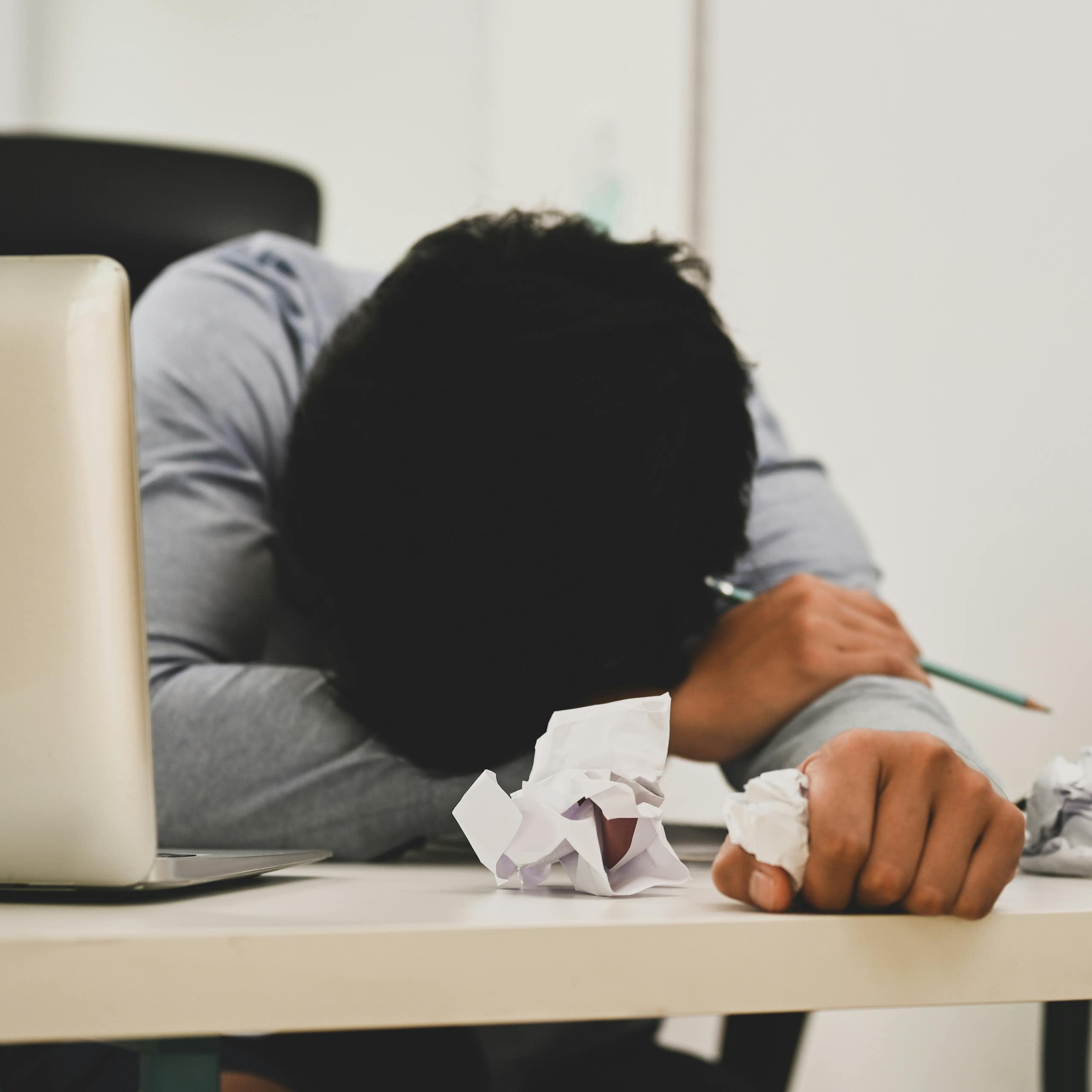 A person resting their head down on their arms while sitting at a desk