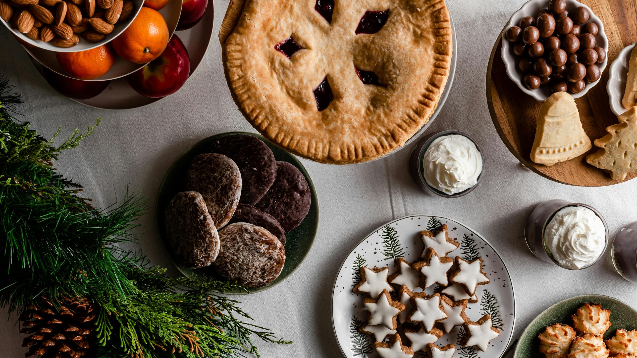 A selection of desserts, fruit and nuts on a table with an evergreen branch