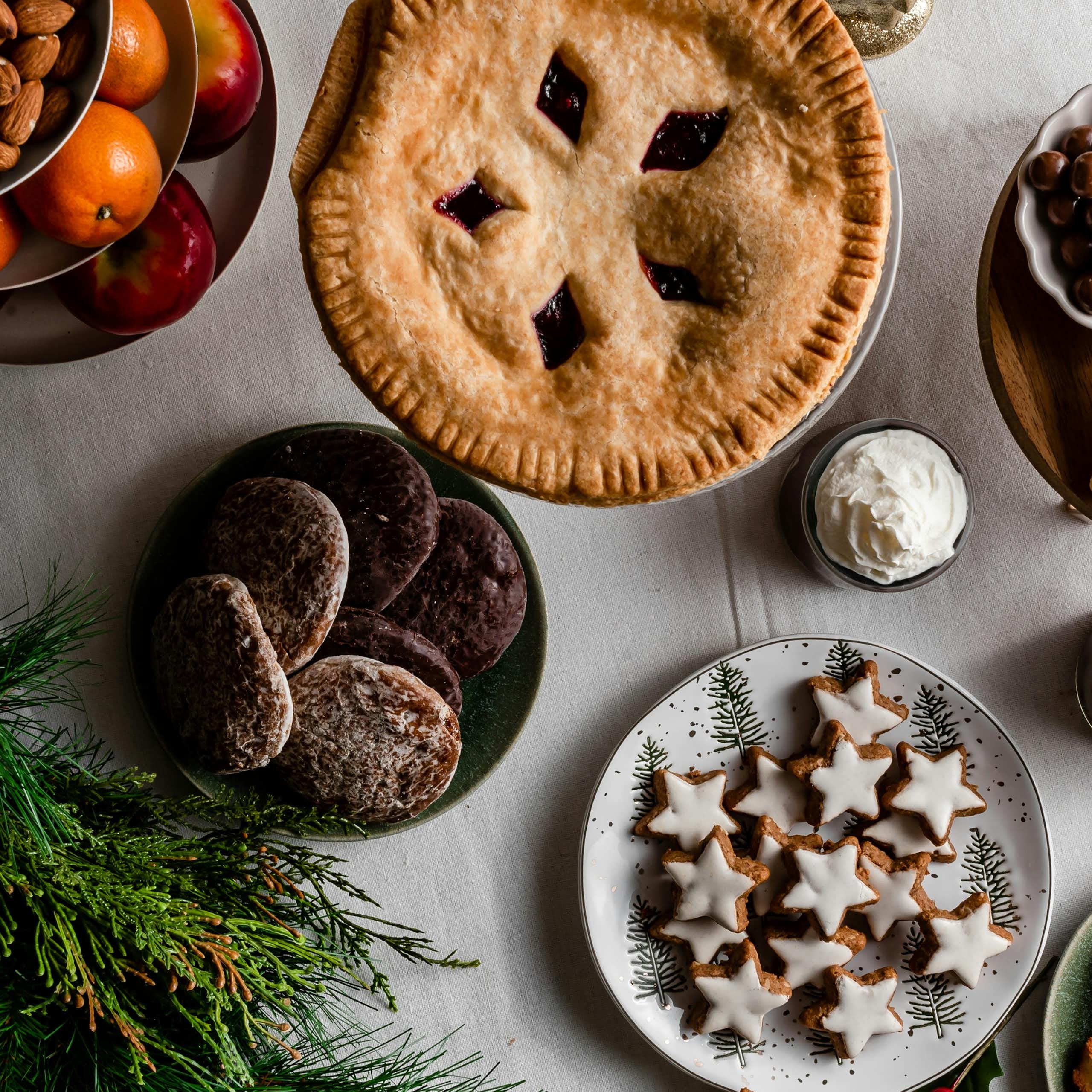 A selection of desserts, fruit and nuts on a table with an evergreen branch