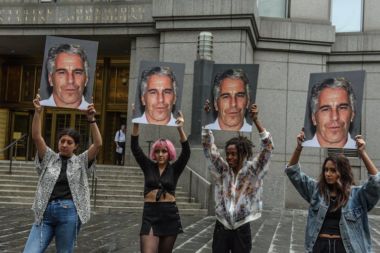 Four women hold photos of Jeffrey Epstein aloft.