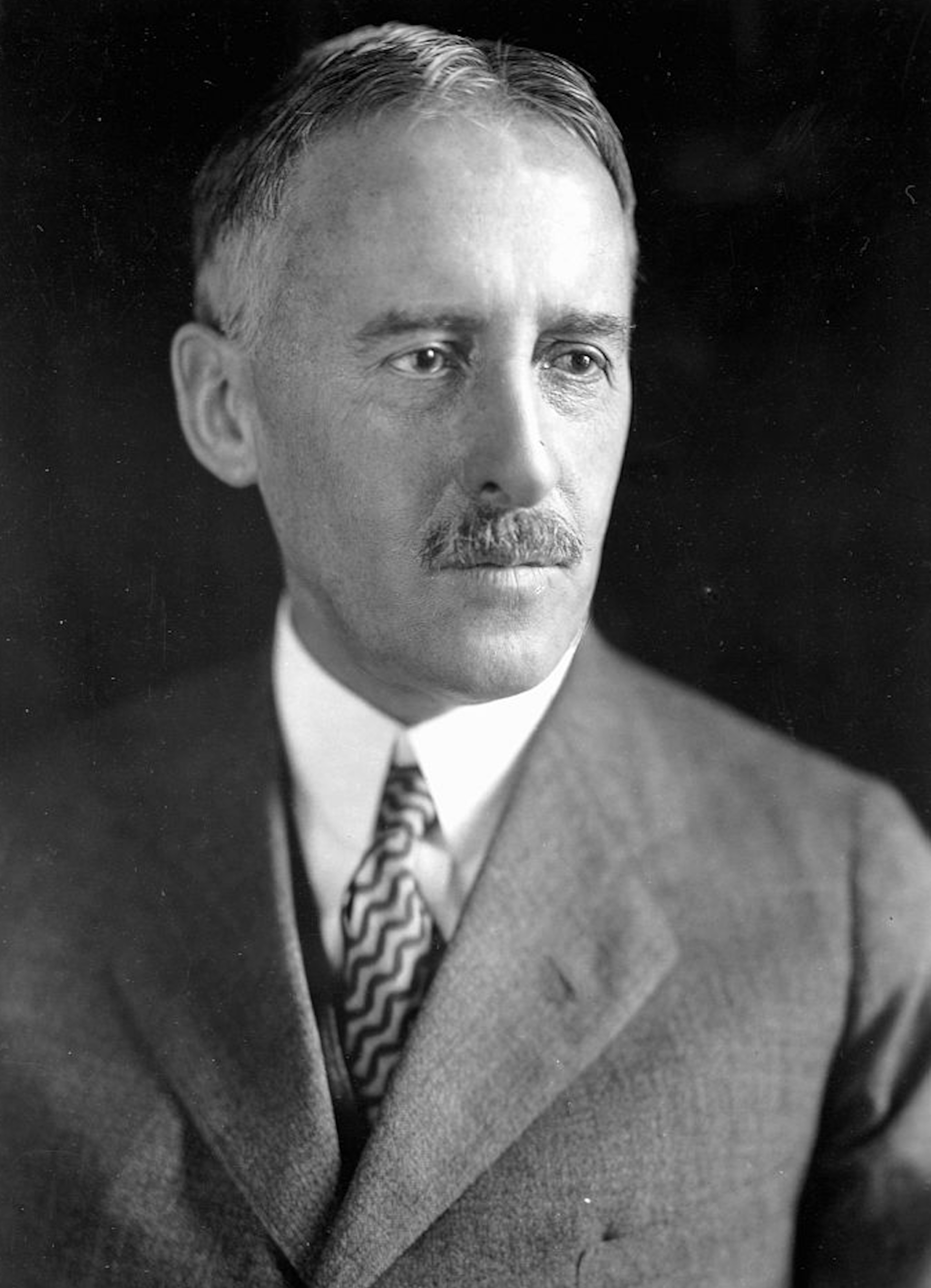 Black-and-white portrait of man with mustache wearing a suit and tie.