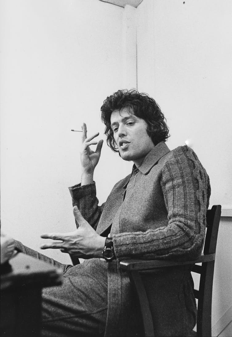 Stoppard sitting at a table and smoking a cigarette.