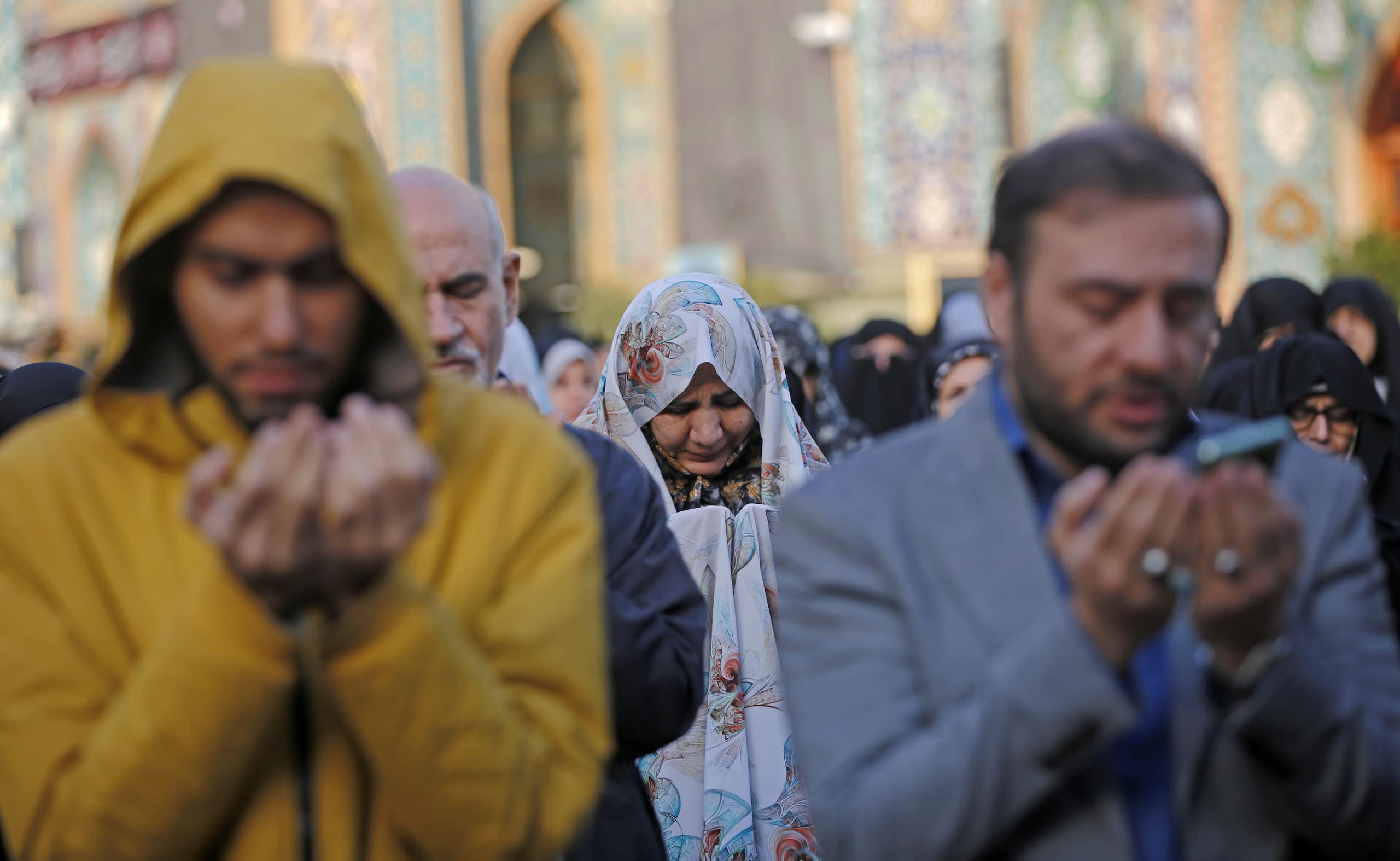 A large group of men and women pray outside.