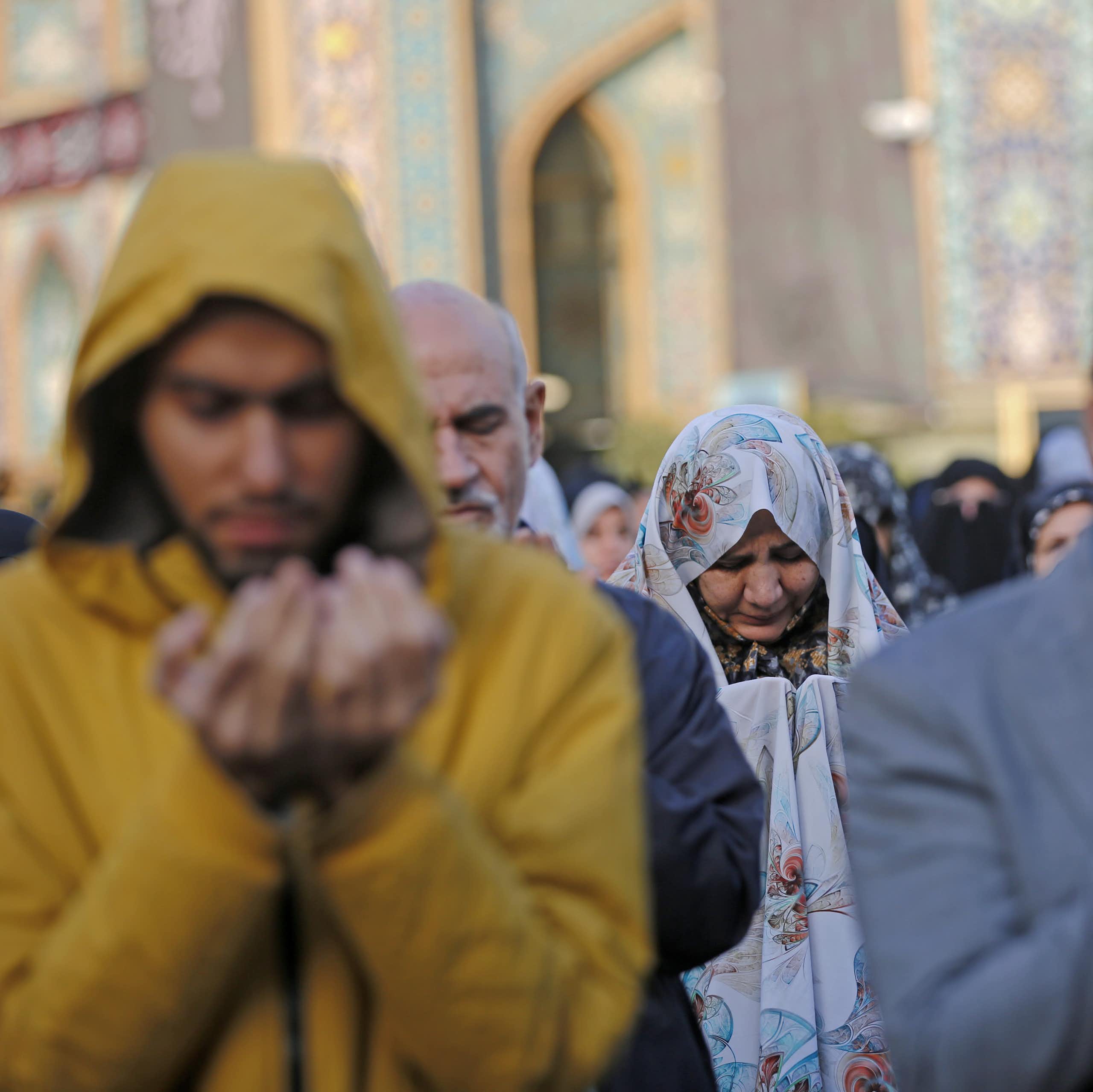 A large group of men and women pray outside.