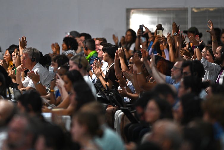 A crowd of people in a large room raise their arms in the air and applaud.