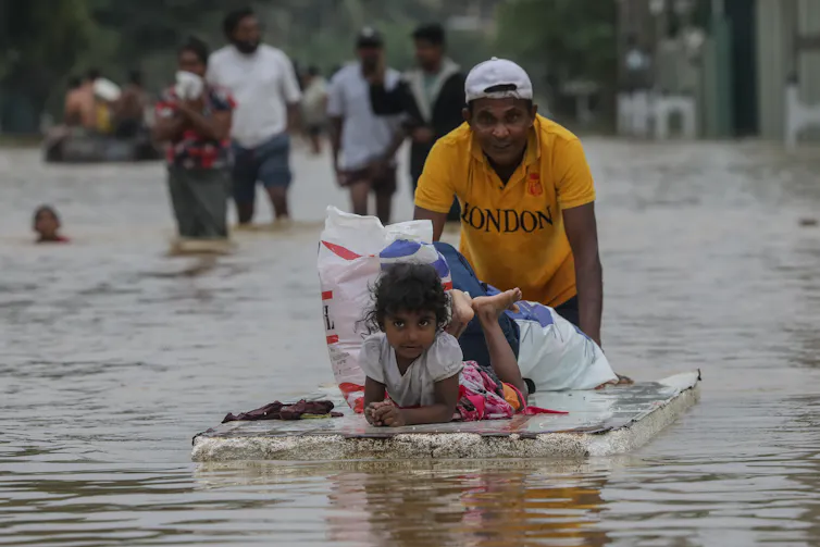 Seorang pria mendorong pintu apung yang membawa putrinya melintasi air banjir.