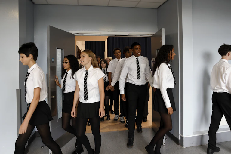 Teenage students in school uniform walk out of a hall.