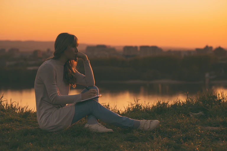 A woman looking pensive writing poetry at sunset