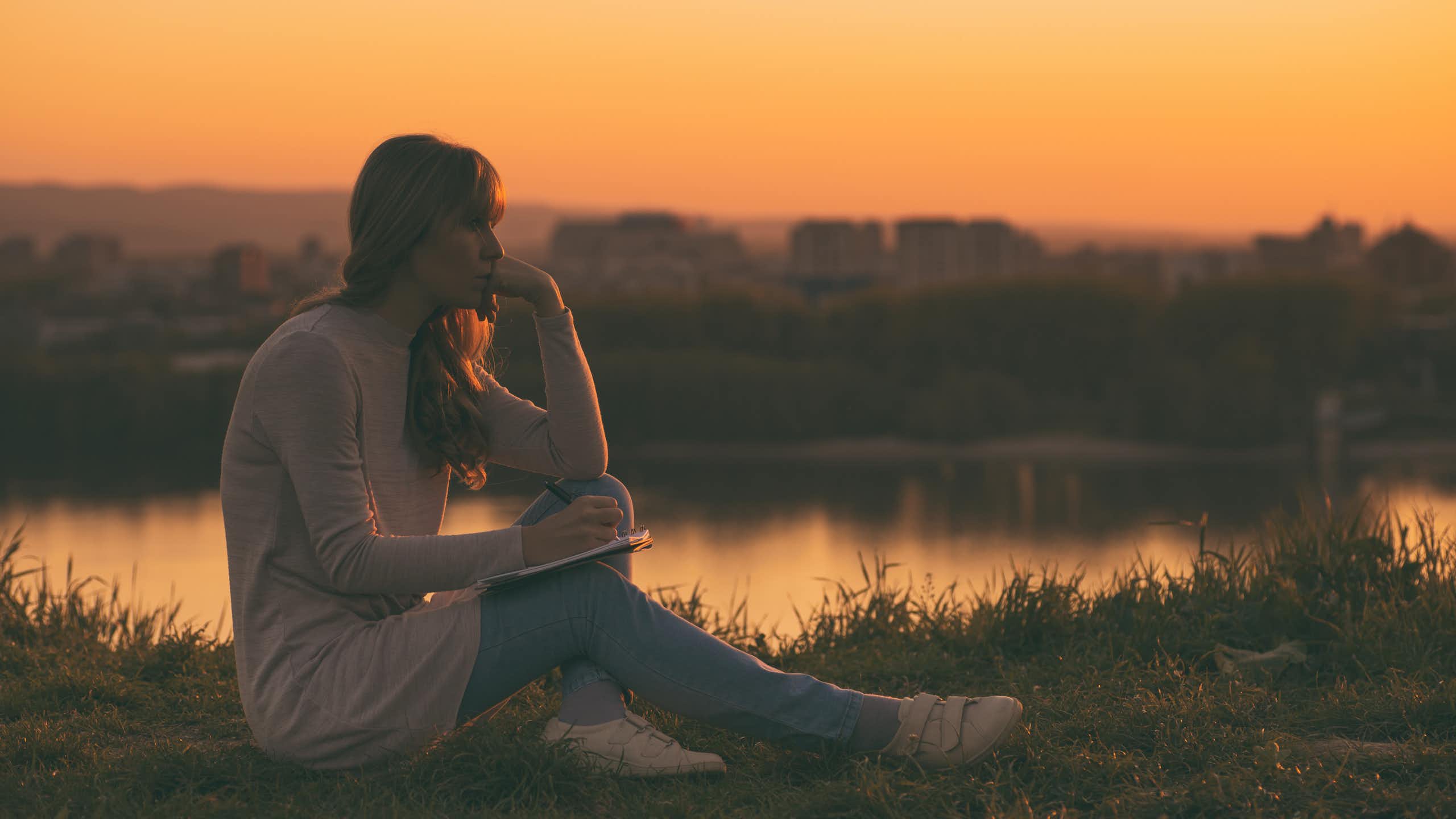 A woman looking pensive writing poetry at sunset
